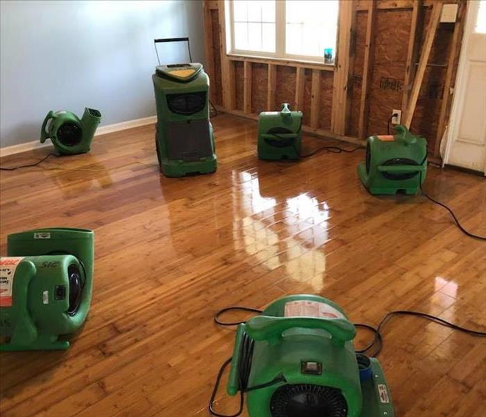 Image shows green SERVPRO drying equipment in a living room with hardwood floors.