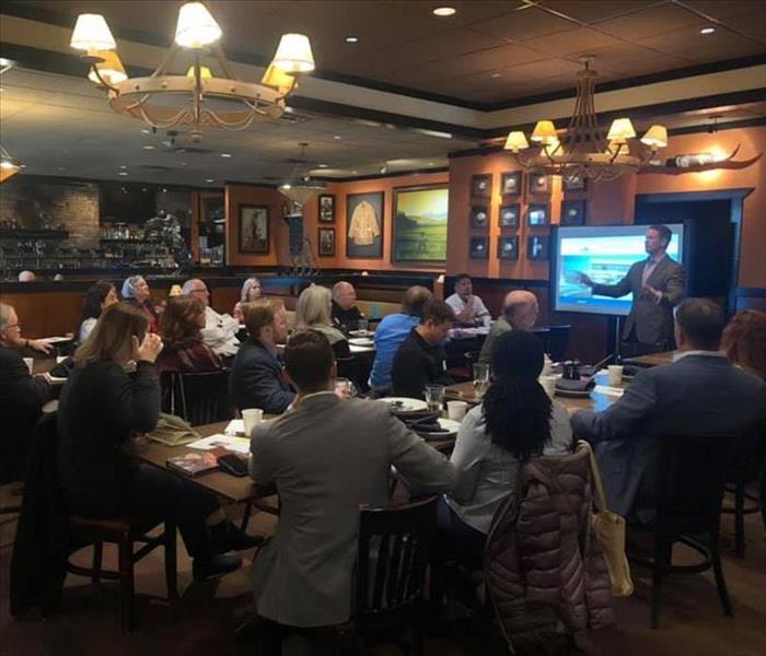 Image shows a group of people at a restaurant listening to a presentation.
