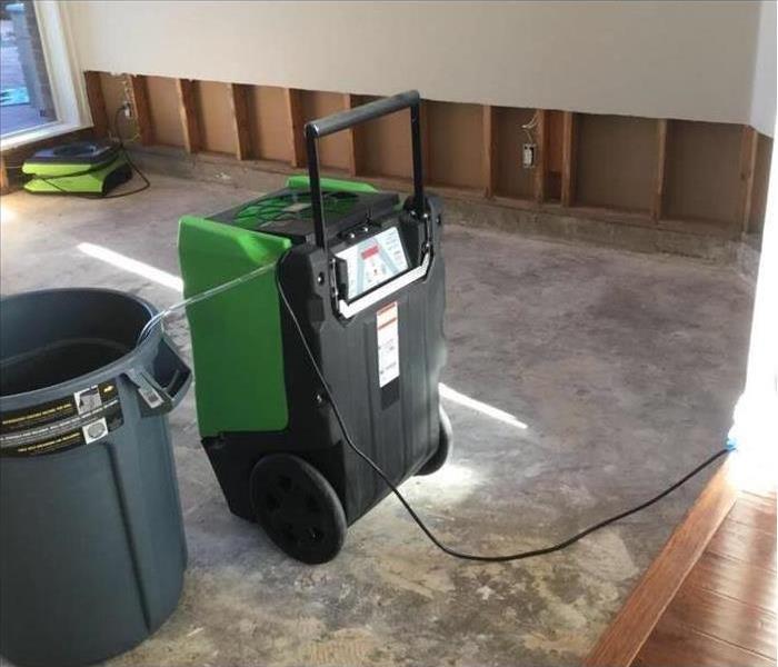 Image shows green SERVPRO dehumidifier in a home where a portion of wall and carpet has been removed due to flood damage.